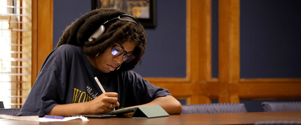 student writing on ipad inside a room, with her headphones on